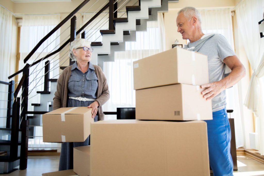 Avoid peak moving season - Happy couple carrying cardboard boxes while moving to a new home